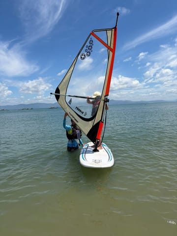 Alumno sosteniendo la vela de windsurf en el agua durante la clase en Ponta das Canas