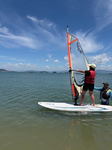 Alumno practicando windsurf con el instructor cerca, con la bahía al fondo