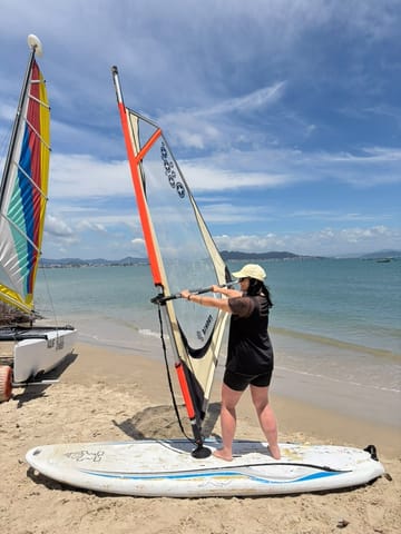 Alumna sosteniendo la vela de windsurf en la arena de la playa de Ponta das Canas