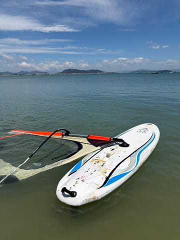 Tabla y vela de windsurf sobre el agua poco profunda, equipo usado en la clase
