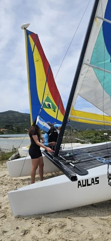 Alumna junto a la vela colorida de un catamarán Hobie Cat en la playa antes de la clase de vela
