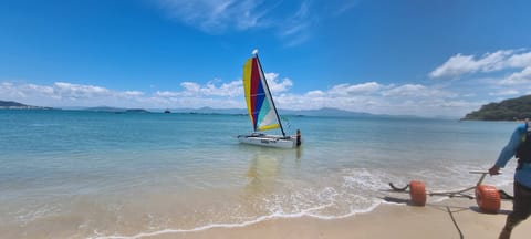 Catamarán Hobie Cat con velas de colores en aguas claras y poco profundas cerca de la playa
