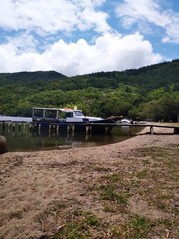 Barco ancorado em trapiche de madeira na Costa da Lagoa, com morros verdes ao fundo
