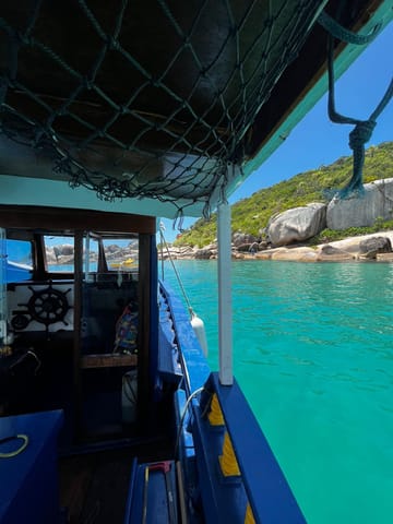 Vista da cabine do barco com águas turquesa e costão rochoso ao fundo