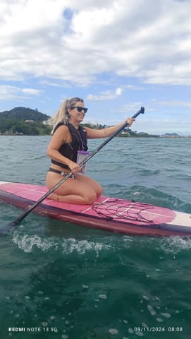 Woman paddling on her knees on a pink stand-up paddle board in the sea off Florianópolis