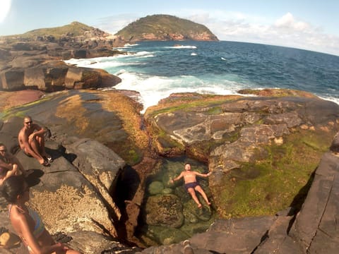 Pessoa boiando em piscina natural entre rochas, com a Ilha das Aranhas ao fundo